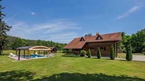 A wooden house with a swimming pool, covered patio, and well-maintained lawn.