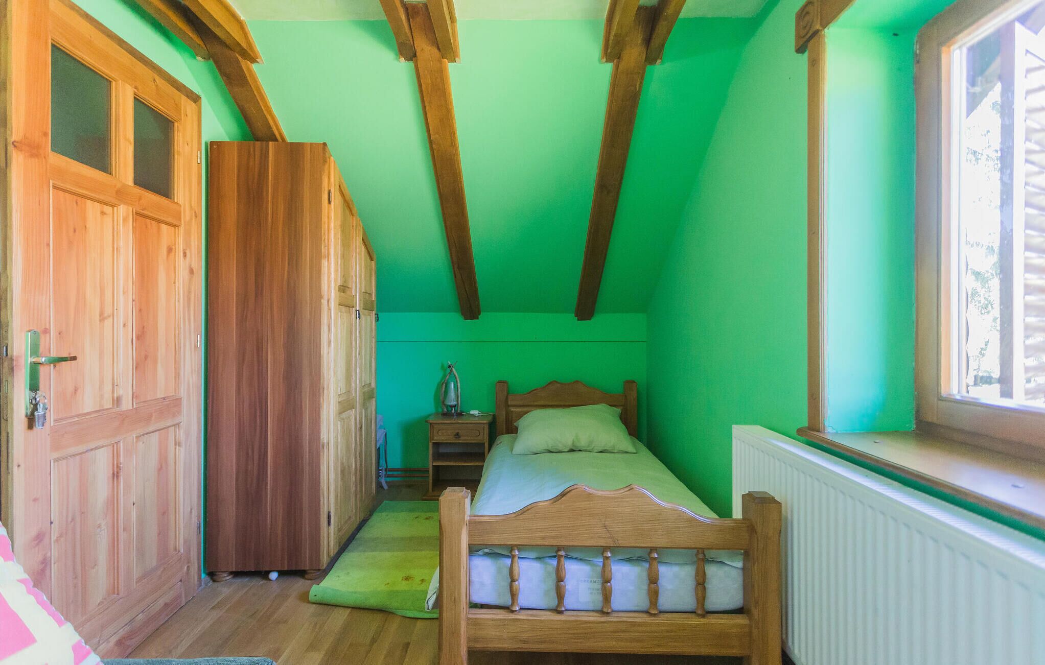 Un dormitorio con una cama de madera, una mesita de noche, una pared verde y una ventana.