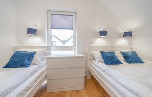 A bedroom with two beds, a nightstand, a window with blinds, and wall-mounted lights. - Cozy home in Rewal with heated swimming pool (Rewal)