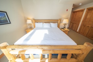 A large bed with a wooden headboard, two bedside tables with lamps, and wooden closets. - Red Hawk Townhomes 2342 (Keystone)