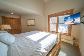 A bedroom with a bed, a wooden wardrobe, a mirror, and a TV displaying a skier. - Red Hawk Townhomes 2342 (Keystone)