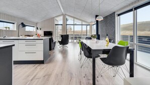 Una cocina moderna con una isla grande, un comedor con mesa y sillas, y amplios ventanales que ofrecen vistas al exterior.