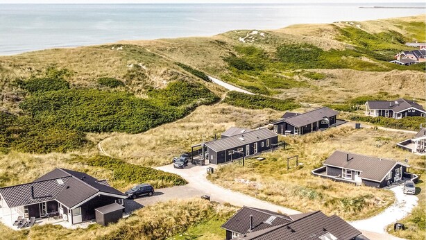 Un área residencial costera con casas de arquitectura moderna, un sendero de tierra y vistas al mar.