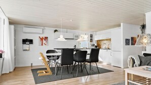 Ett modernt kök med vita skåp, en matplats med svarta stolar och en trägitarr som ligger på en matta.
