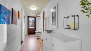 En hall med en vit vägg, trägolv och ett vitt konsolbord med ett ljus och en växt.