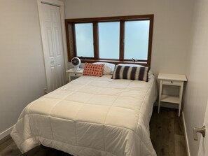 Une chambre à coucher comprenant un lit, une table de chevet, une commode, une fenêtre et une porte.