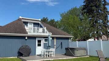 Une maison avec une terrasse, un barbecue couvert et un jacuzzi.