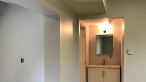 Un pasillo con piso de madera, una puerta blanca y un baño con lavamanos y armarios.