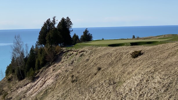 Paisaje costero con un campo de golf, árboles y vistas al mar.