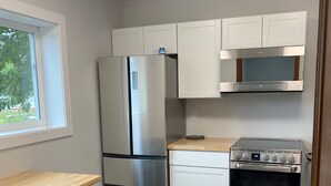 Una cocina compacta con refrigerador, horno, microondas y gabinetes blancos.