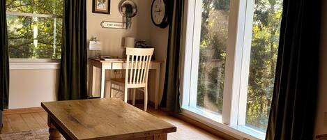 A room with a wooden table, a white chair, a desk, and a large window with curtains.