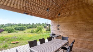 An outdoor wooden deck with a table and chairs, a grill, and hanging lights. - 3 bedroom gorgeous home in Silkeborg (Silkeborg)