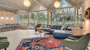 A spacious room with a large dining table, a sofa, and a coffee table. There are large windows providing a view of the outdoors. - 3 bedroom gorgeous home in Silkeborg (Silkeborg)