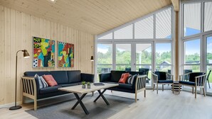 Un salon moderne avec un plafond en bois, de grandes fenêtres, un canapé en cuir noir, une table basse en bois et deux fauteuils.