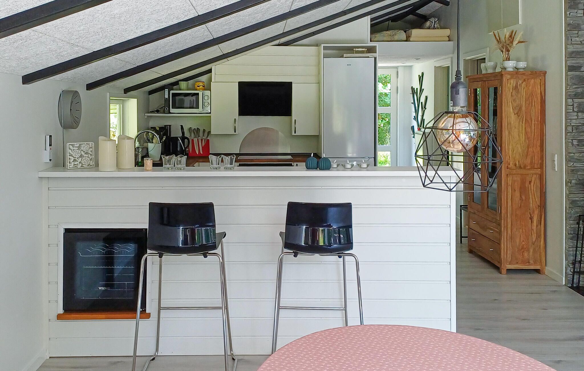 Una cocina compacta con microondas, tostadora y lavamanos. Hay dos taburetes de bar y un armario de madera.