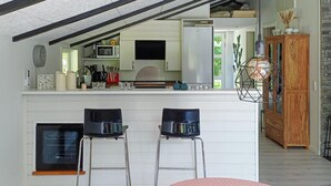 Una cocina compacta con microondas, tostadora y lavamanos. Hay dos taburetes de bar y un armario de madera.