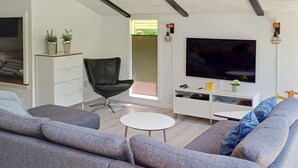 Una sala de estar moderna con un sofá gris, un sillón negro, una mesita blanca, un televisor montado en la pared y un mueble blanco con estantes.