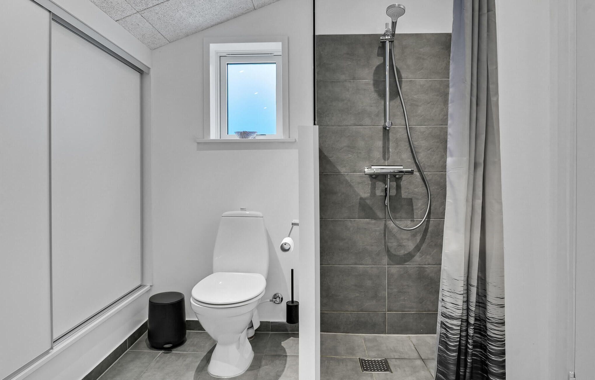 A modern bathroom with a toilet, a shower, and a window.