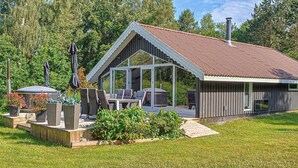 Una casa moderna con un amplio ventanal de vidrio, mobiliario para exteriores y un jardín cuidado.