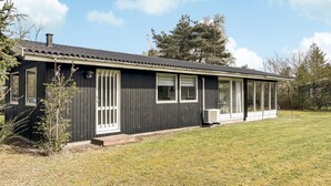 En enplansbyggnad med en mörk fasad, stora fönster och en täckt veranda.