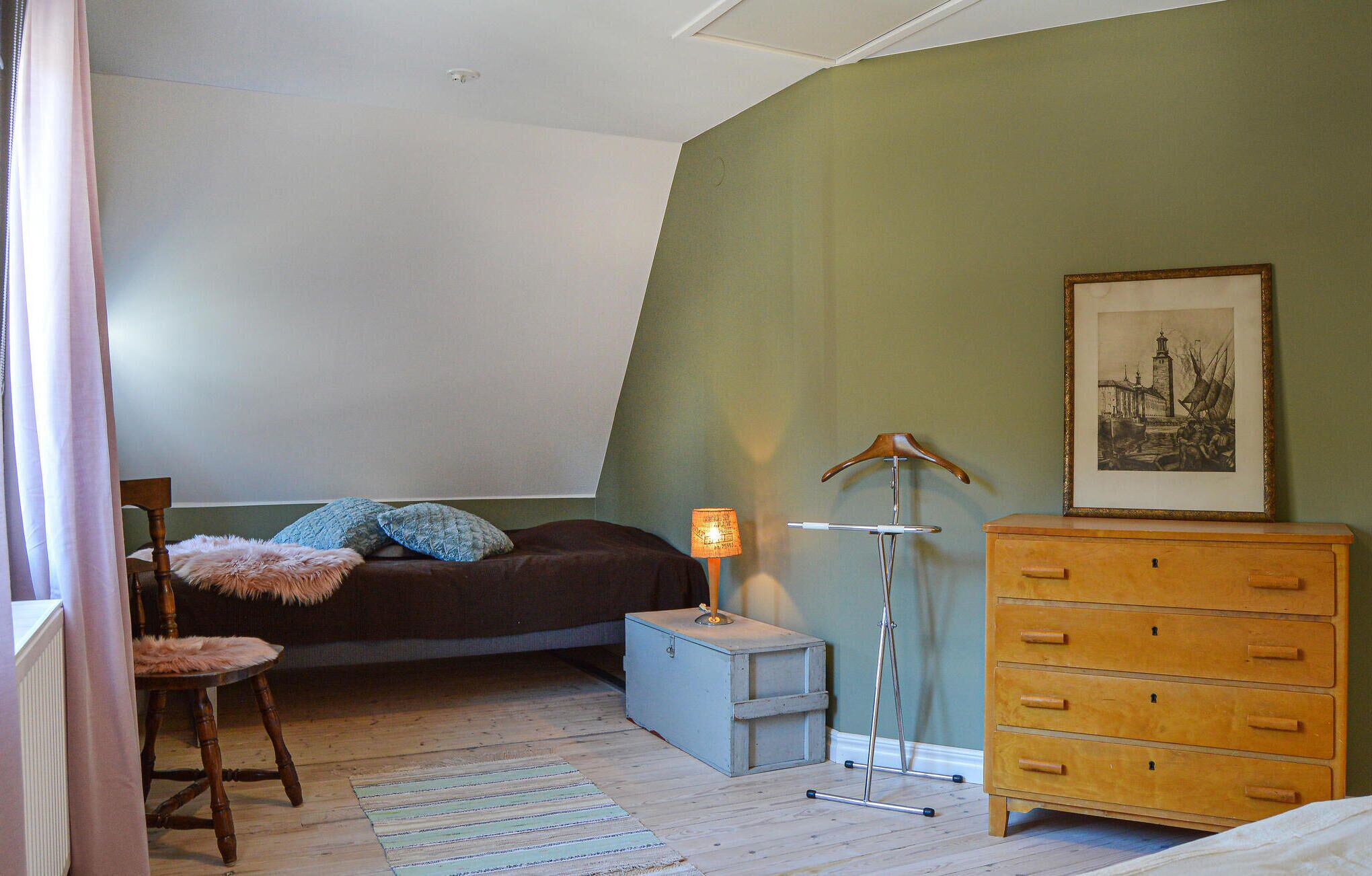 Une chambre à coucher avec un lit, une commode, une chaise, une lampe et un tableau encadré au mur.