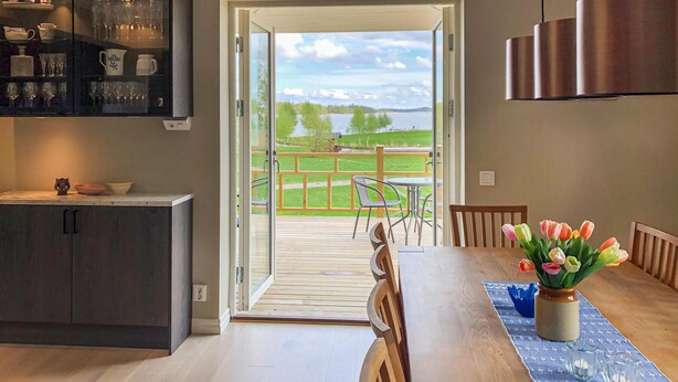 A dining area with a wooden table, chairs, and a view of a deck and lake. - Gorgeous home in Strängnäs with sauna (Strängnäs)