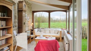 Une pièce chaleureuse avec un mur en pierre, des meubles en bois, un canapé blanc et une vue sur un champ verdoyant.