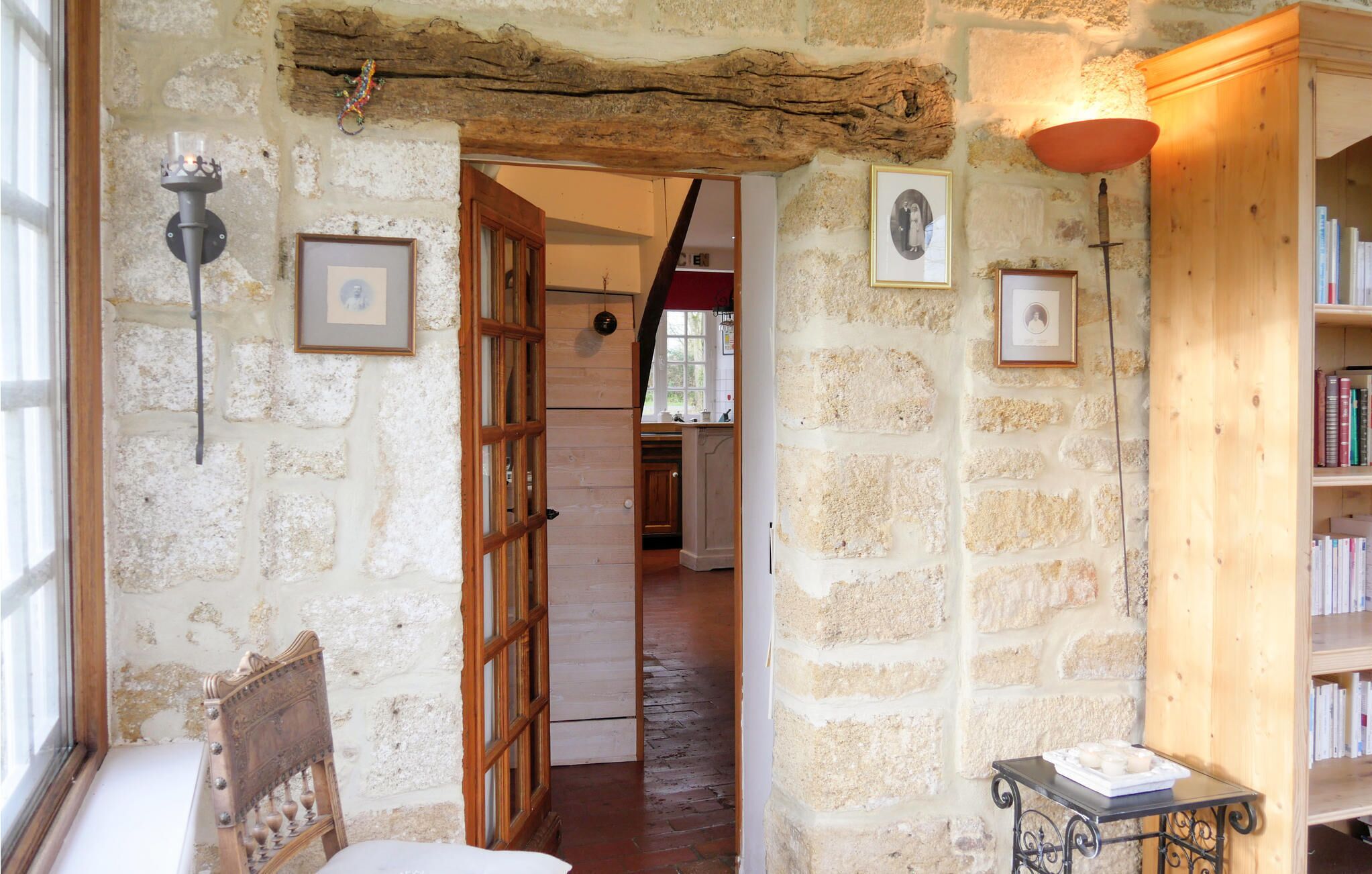 Un pasillo de paredes de piedra que lleva a una cocina, con una silla de madera y una pequeña mesa con velas.
