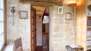 Un couloir aux murs de pierre menant à une cuisine, avec une chaise en bois et une petite table sur laquelle sont posées des bougies.