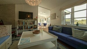 A living room with a sofa, a coffee table, a bookshelf, a television, and a window with a view. - Lovely home in Anholt with WiFi (Anholt)