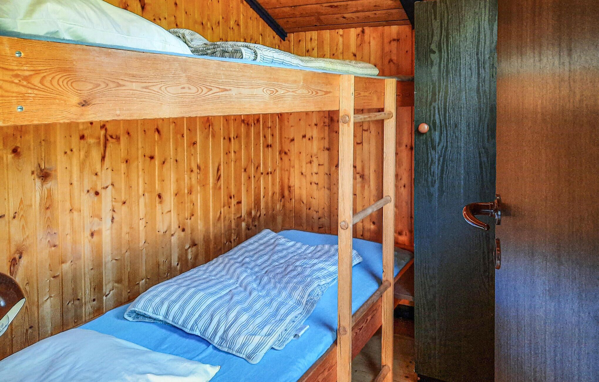 A bunk bed room with a wooden bunk bed, a blue mattress, and a wooden wardrobe with a door.