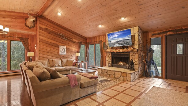 A cozy log cabin interior with a stone fireplace, a large sectional sofa, and a television mounted on the wall. - COZY MOUNTAIN ESCAPE! .5mi frm slopes 50ft to trails. HOT TUB! (Beech Mountain)