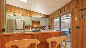 A kitchen with wooden cabinets, a refrigerator, a microwave, and a bar area with two chairs. - COZY MOUNTAIN ESCAPE! .5mi frm slopes 50ft to trails. HOT TUB! (Beech Mountain)