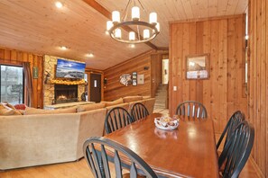 A cozy cabin interior with a stone fireplace, wooden walls, a dining table, and a sofa.