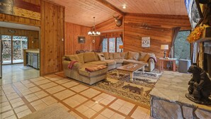 A log cabin interior with a large sectional sofa, a stone fireplace, and a dining area with a view of the outdoors. - COZY MOUNTAIN ESCAPE! .5mi frm slopes 50ft to trails. HOT TUB! (Beech Mountain)