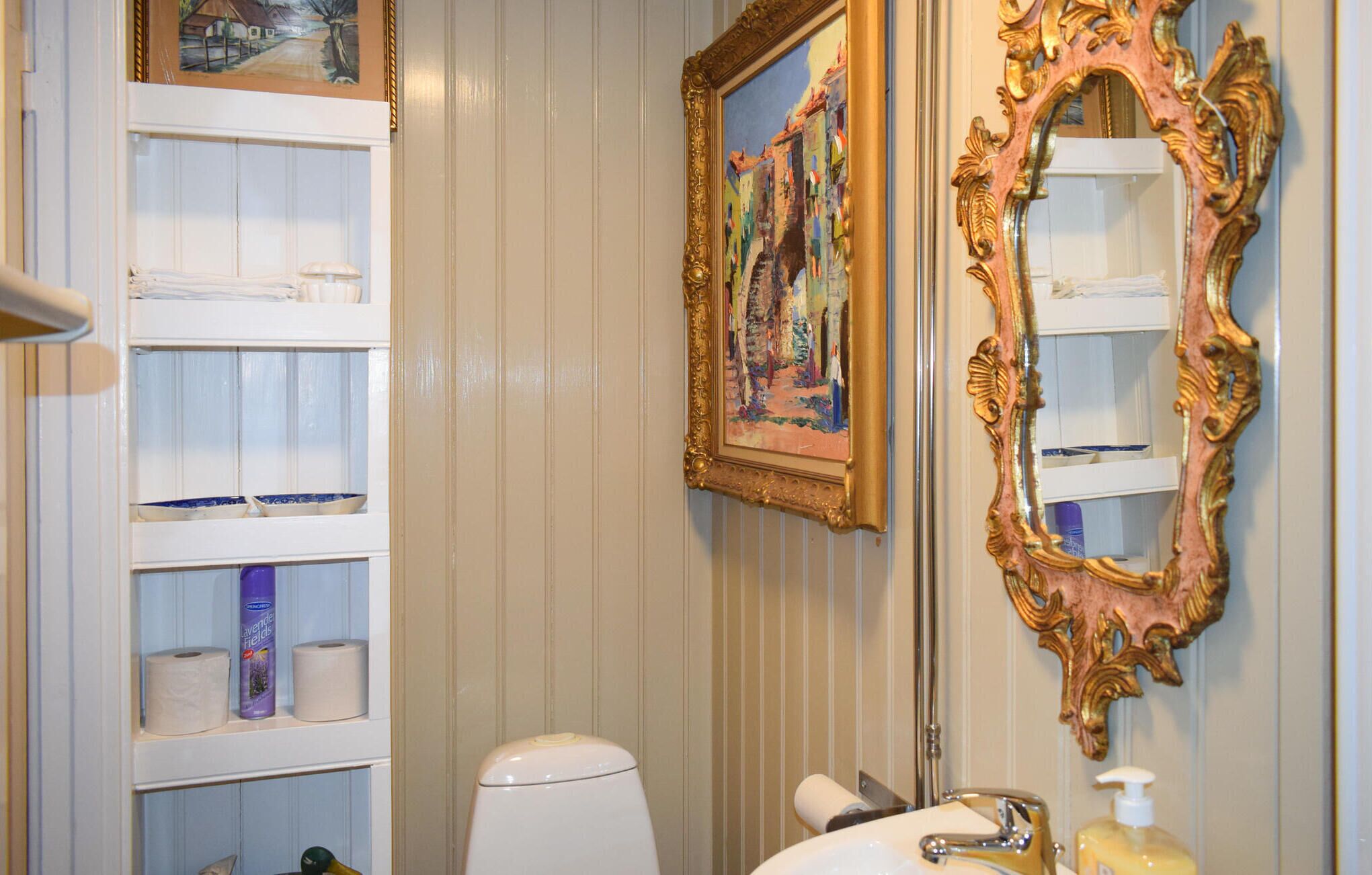 A bathroom with a toilet, sink, and shelves with toiletries.