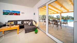 En moderne stue med en modulsofa, et sofabord og en stor skydedør, der fører ud til en udendørs terrasse med en pool.
