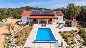 Et toetagers hus med rødt tegltag, solpaneler, en swimmingpool og et grillområde i sten.