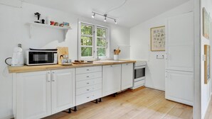 A modern kitchen with white cabinetry, a wooden countertop, a built-in oven, and a window providing natural light. - Beautiful home in Melby with kitchen (Melby)