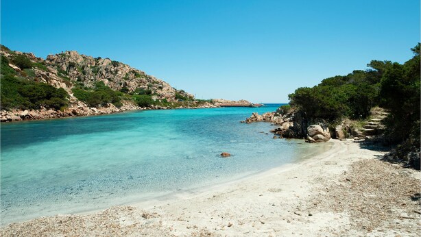 Een kuststrand met helder turquoise water, rotskliffen en een zandstrand.