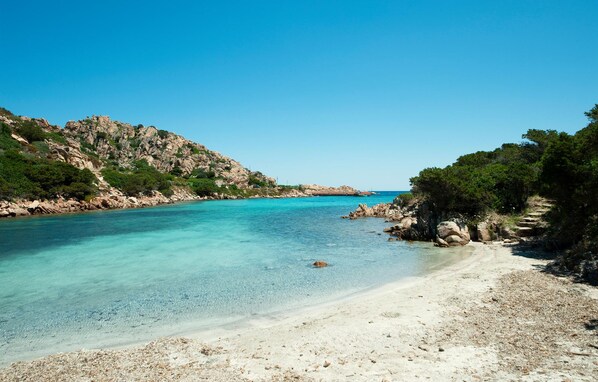 Une plage côtière aux eaux turquoise et limpides, bordée de falaises rocheuses et d’un rivage sablonneux.