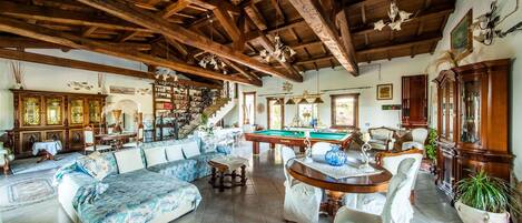 A spacious living room with a pool table, a sofa set, and a staircase leading to an upper level.