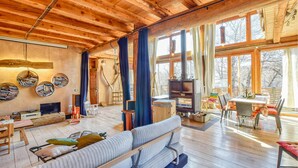 A cozy cabin interior with a wooden ceiling, a fireplace, a sofa, a dining table, and a TV.