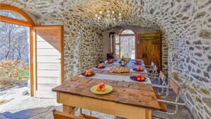 A rustic stone-walled dining area with a wooden table set for a meal, surrounded by metal chairs.