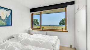 Une chambre avec une grande fenêtre donnant sur la mer et les arbres.