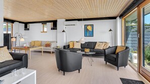 Un salon moderne avec un plafond en bois, des canapés en cuir noir, une table à manger et une grande fenêtre donnant sur l’extérieur.