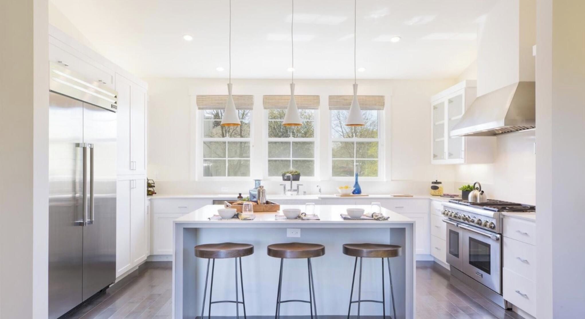 A modern kitchen with a central island, bar stools, stainless steel appliances, and large windows.