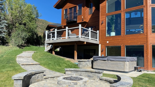 Uma casa de madeira de dois andares com varanda, lareira de pedra e banheira de hidromassagem.