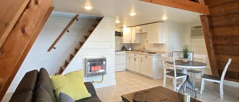 Une pièce de style loft avec un plafond en bois, un canapé, une table basse et un coin cuisine visible grâce à un espace ouvert.