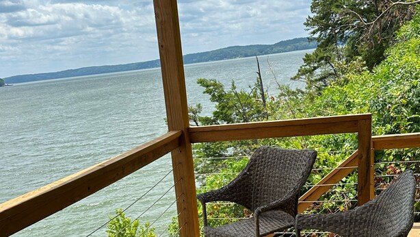 Eine Holterrasse mit Korbmöbeln und einem Tisch mit Blick auf ein Gewässer.